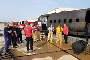 A group of Aircraft Rescue and Fire Fighting Unit personnel standing around Simulated Aircraft Fire Equipment Trainers