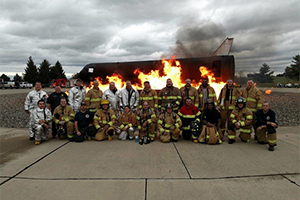 A group of Aircraft Rescue and Fire Fighting Unit personnel standing in front of Simulated Aircraft Fire Equipment Trainers