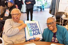 two women holding a bag that says Bring Your Own Bags