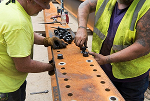 Two construction workers inserting bolts into a bridge platform.