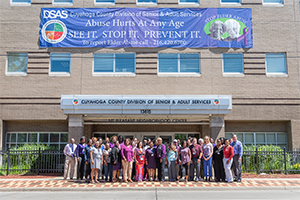 A group of Cuyahoga County Division of Senior and Adult Services professionals standing in front of a banner that reads Abuse hurts at any age. See it. Stop it. Prevent it