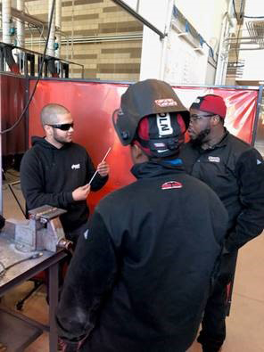 man shows welding peice to two welding students