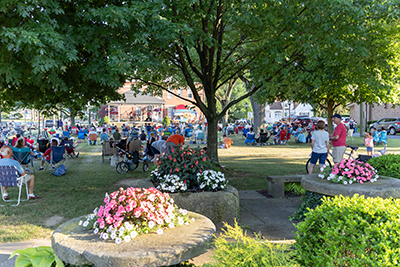  In a park like setting, a small crowd of people is listening to a band performing in a gazebo.