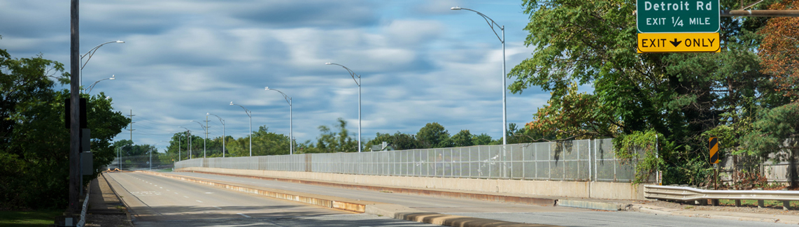 A two-lane roadway overpass with a large exit sign above the right side of the road.