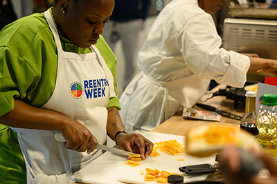 Woman wearing Reentry Week apron while slicing food on cutting board.
