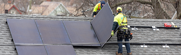 On the roof of a house, two workers are installing solar panels.
