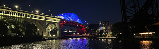 A bridge span over water at night is illuminated in red, white, and blue lighting.