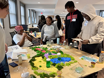 Fiveyoungpeoplearestandingaroundatablethathasaterraindisplaywithliquidvialsonit