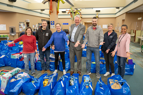 Group of people smiling and showing off a room full of blue gift bags.