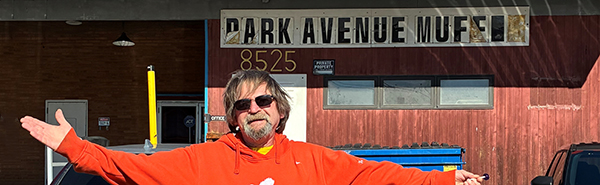 Man in orange hoodie standing in front of his small business.