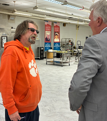 Man in a orange hoodie talking to another man in a grey suit.