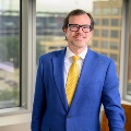 Amaninabusinesssuitwearingglassesissmilinginanoffice