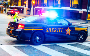 Close-upofaCuyahogaCountySheriffsvehiclewithemergencylightsflashingatnightTheredandbluelightsreflectoffthecarssurfacecreatingadramaticandurgentatmosphere