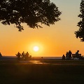 Anorangeskyduringsunsetwithsilhouettesoftreesandpeoplealongashoreline