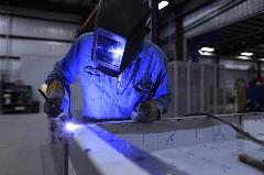 Male wears welder's mask and hold torch while working at bench. 