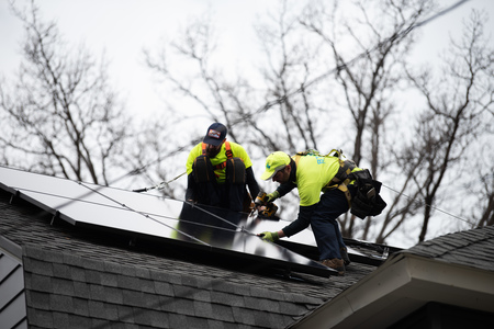 Two men install solar panels on a house in Lakewood. 