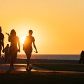 Peoplewalkingonabeachtowardwaterinsilhouettewhilethesunsets