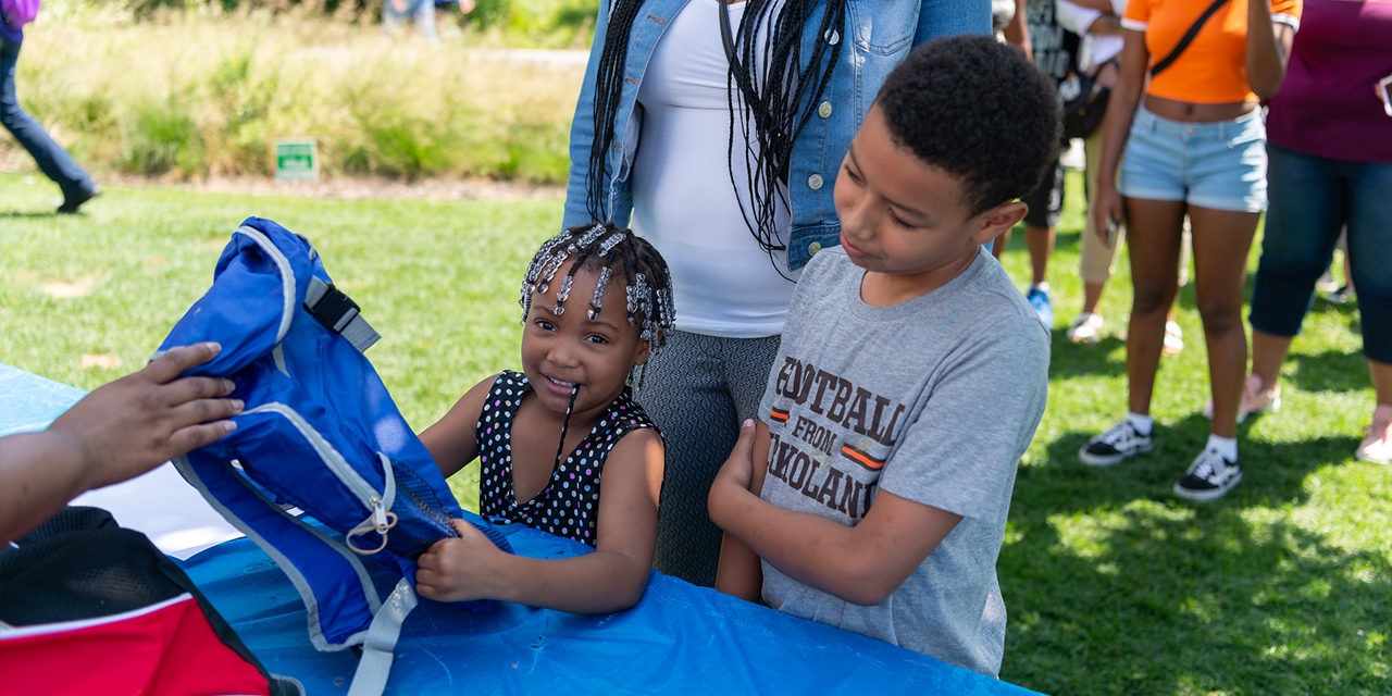 A smiling child receives a new blue backpack at a community event.