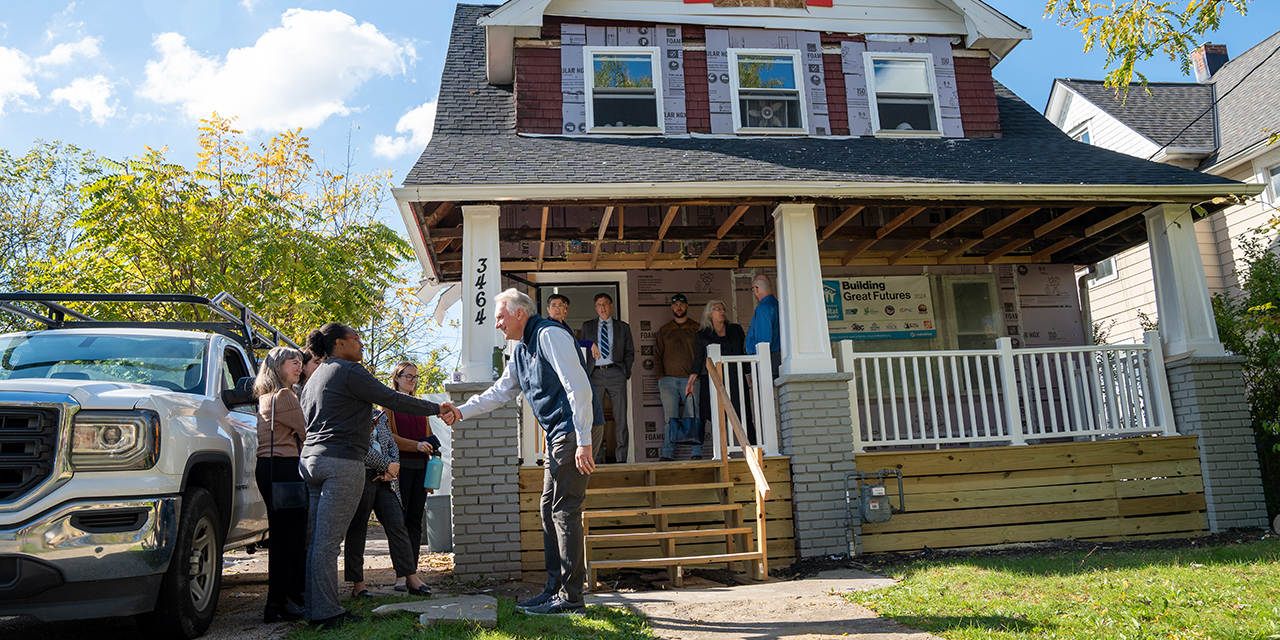 People gather outside a home as two individuals shake hands.