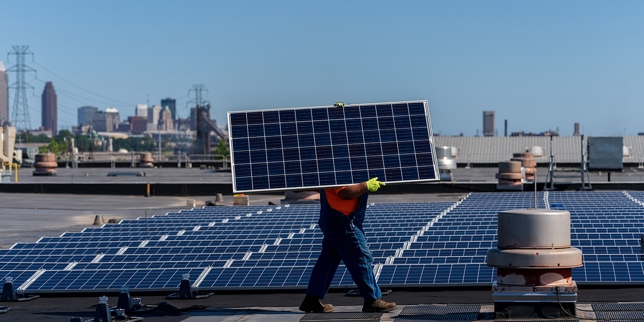 A worker carries a solar panel across a rooftop solar array.