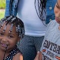 kidgettingabackpackatFamilyFunDayApersonishandinganewbluebackpacktoachildwhoissmilingwithanotherolderchildlookingon