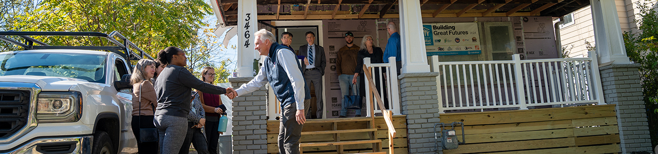 A man is shaking hands with a person in front of a house where people are standing on the front porch
