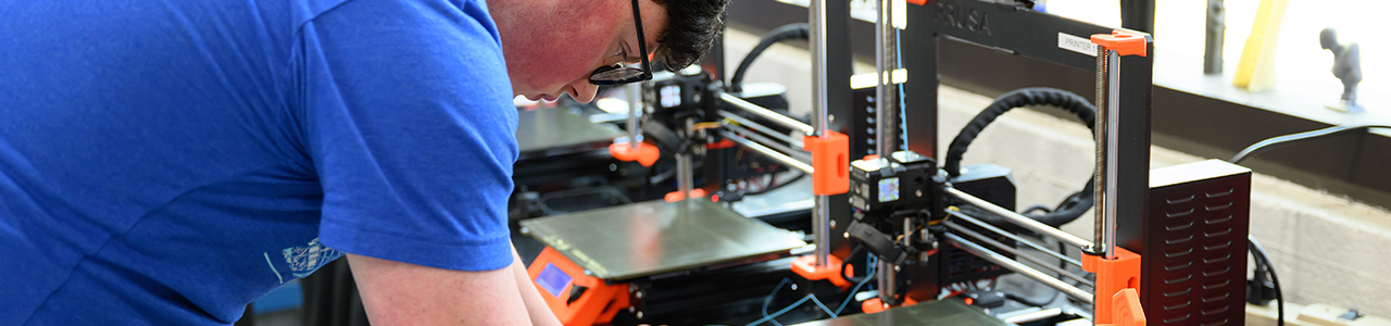 A young man in a t-shirt is calibrating a piece of machining equipment