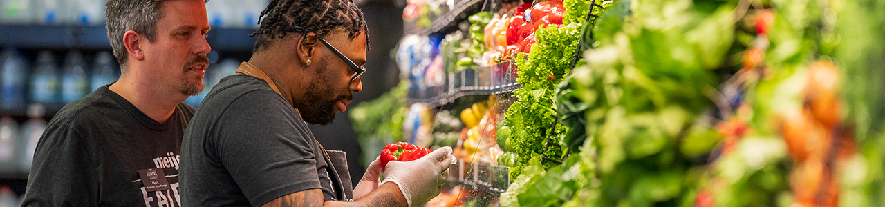 2 men at grocery store produce sections looking at vegetables.