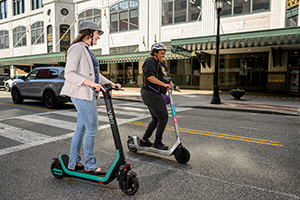 two women riding scooters on a road