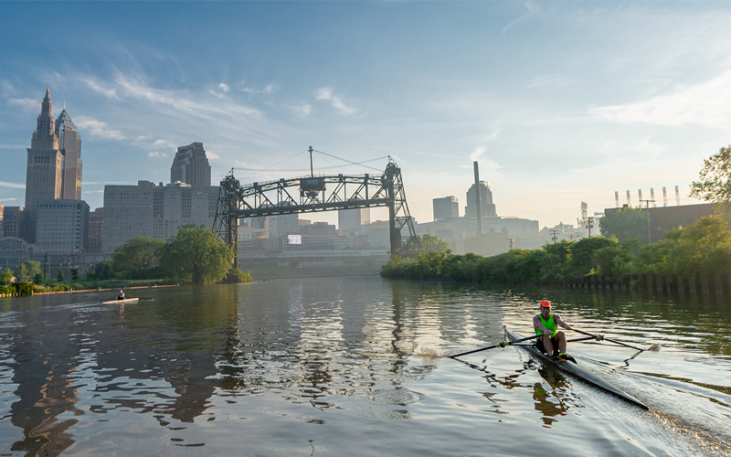 ApersonrowingasinglescullontheCuyahogaRiverwiththeClevelandskylineandtheMainAvenueBridgeinthebackgroundatsunriseorsunset