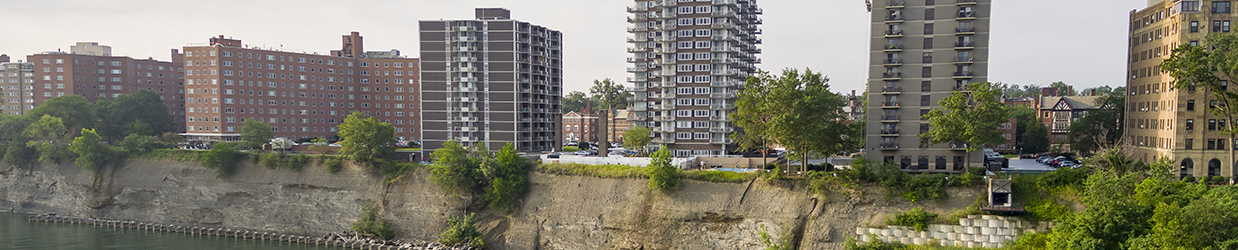 Blue-green water meeting a steep, rocky shoreline with six high-rise buildings.