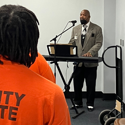 Man standing in front of inmates providing religious services for the residents.