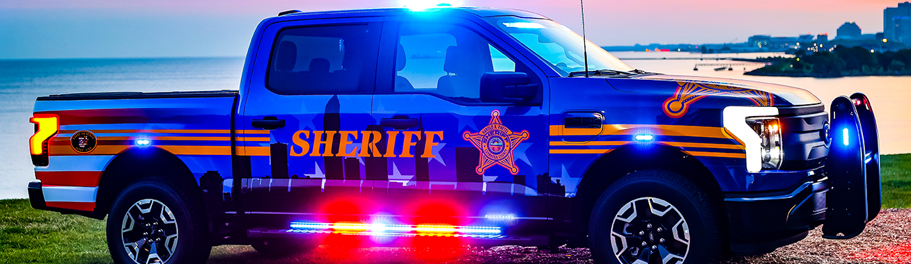 a Sheriff SUV parked on the pier near the lake with a boat in the background