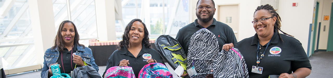 four adults smiling and holding up backpacks