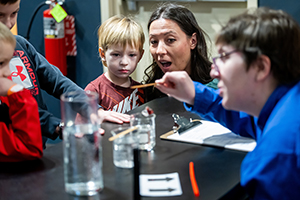 young man performing an experiment at the Great Lakes Science Center while people watch