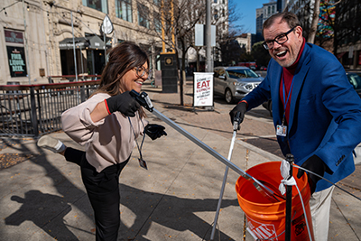 Man holding bucket and woman putting garbage in the bucket with a hand grabber