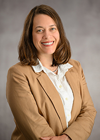Jenita McGowan in a light brown blazer is smiling in a professional pose.