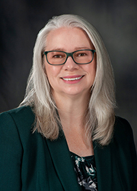 A woman with white hair and glasses is smiling in a posed portrait