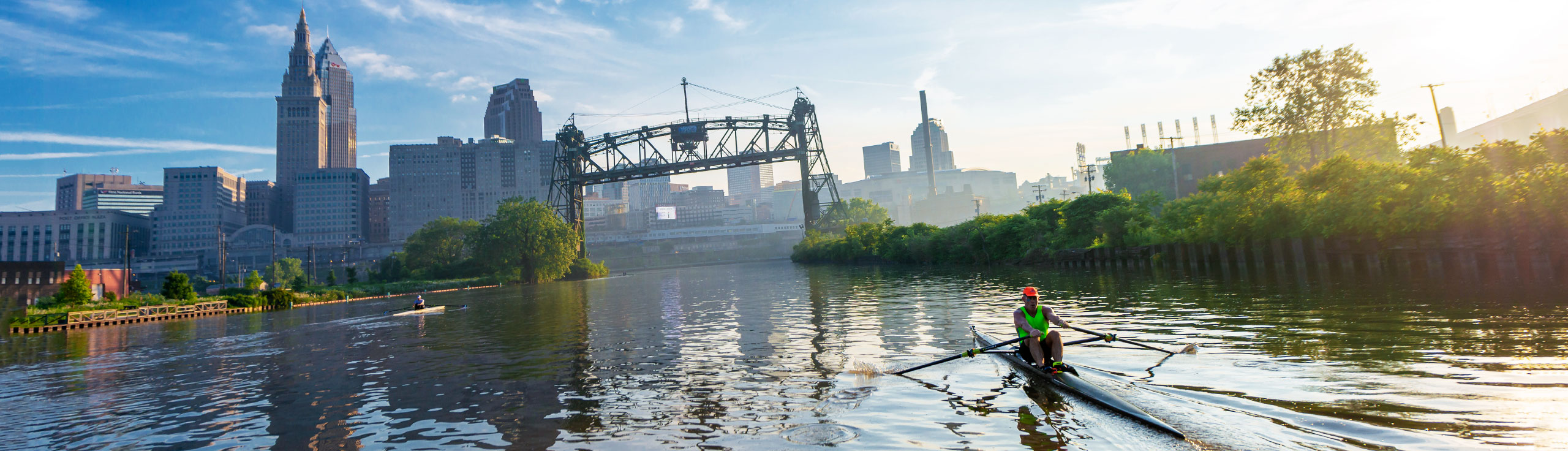 A person in a kayak rowing on the water with downtown Cleveland in the background.