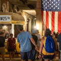 AcrowdofpeoplelookingatahistoricyellowsubwaywithanAmericanflaghangingfromtheceiling